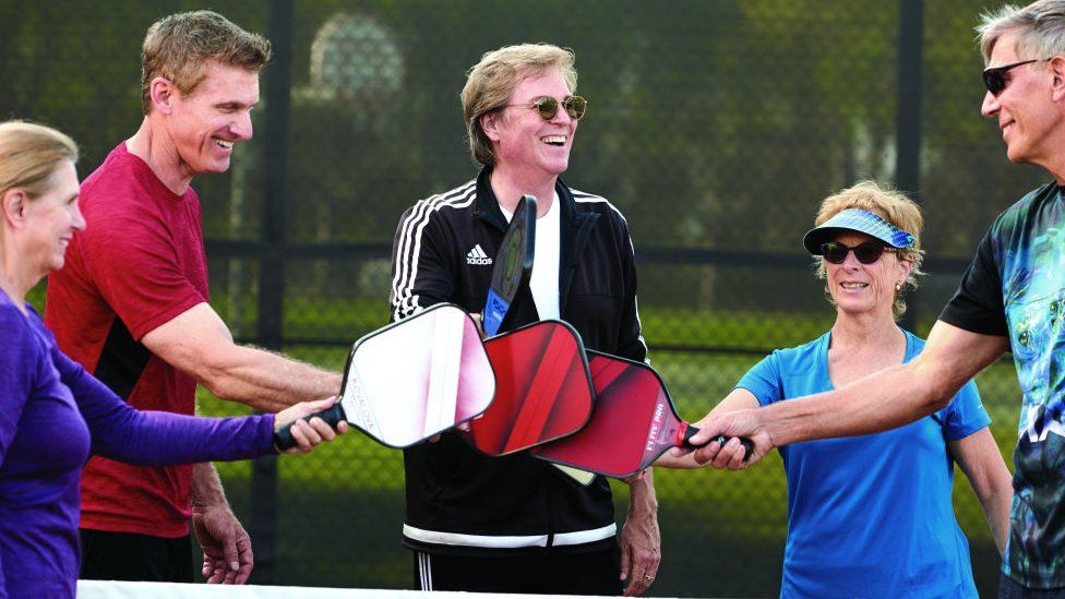 ickleball instructor Mike Fischer, center, congratulates his students after practice on the pickleball courts at Bonita Canyon Sports Park in Newport Beach