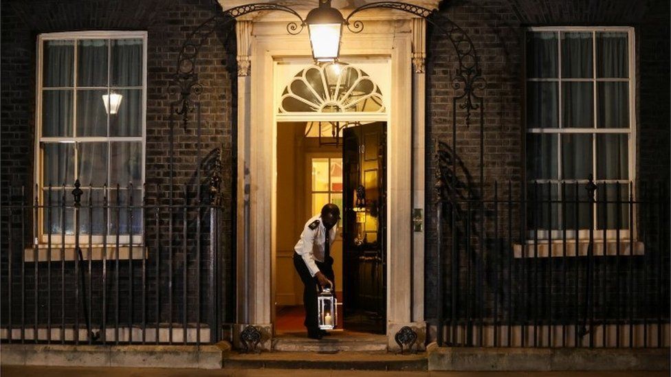 A doorman places a candle on the doorstep of Downing Street